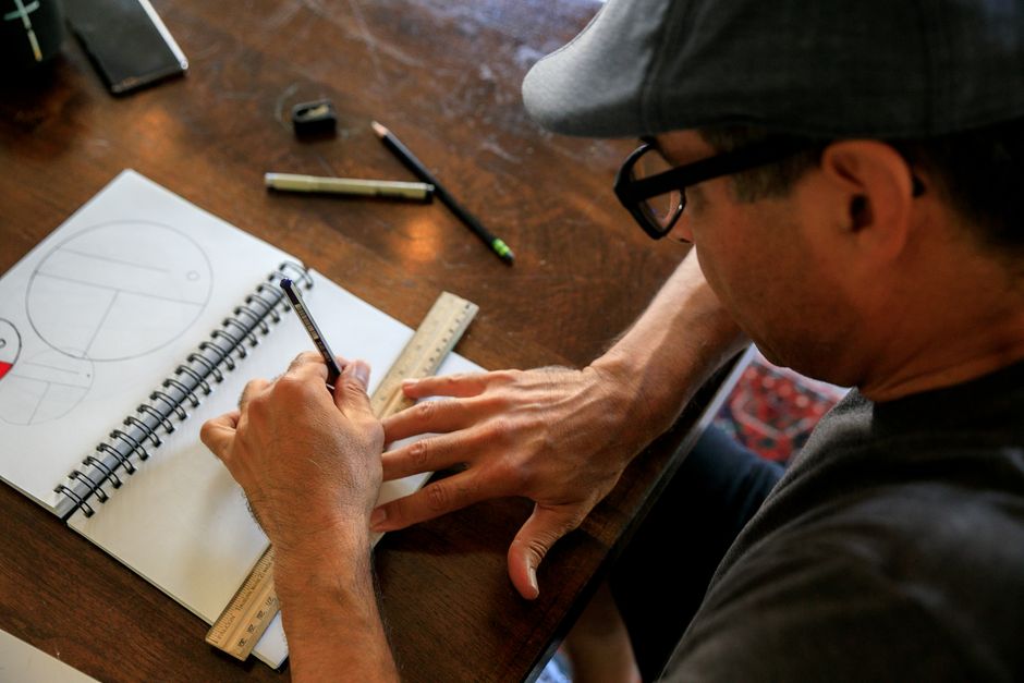 Man drawing geometric shapes in a notebook at a wooden desk, capturing artistic focus.